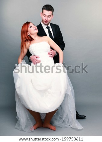 Wedding day. Portrait of happy funny married couple red haired bride and groom in full length studio shot on gray background