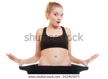 Weight loss, healthy lifestyle. Blonde young happy excited woman fitness girl with big pants, showing how much weight she lost, isolated on white background
