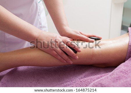 Day-spa. Therapist in work and female leg of customer. Young woman relaxing in healthy beauty spa salon. Girl having hot stone massage. Indoor. Bodycare and relax.
