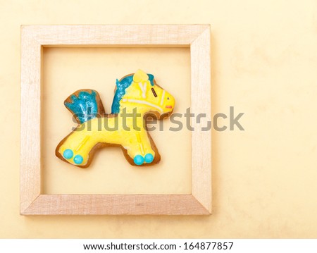 Christmas homemade gingerbread cake pony with icing and blue yellow decoration in wooden frame on brown background. Holiday handmade concept.