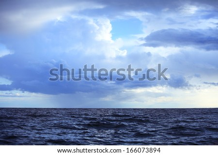 Gray deep blue fluffy thunder clouds stormy sky above a dark surface of the sea. Meteorology
