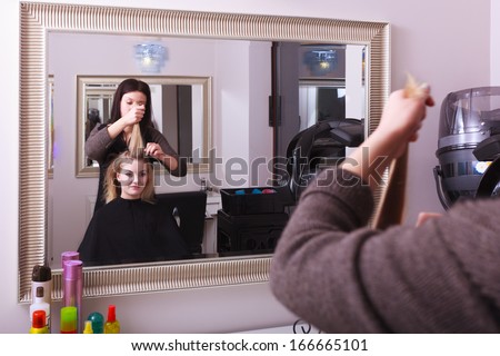 Beautiful young woman in beauty salon. Blond girl with hair curlers rollers by hairdresser. Hairstyle. Reflection in mirror.