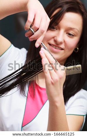 Hairstylist with comb and scissors cutting hair of female client. Woman in hairdressing beauty salon.