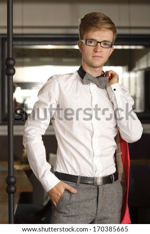 Young handsome stylish man fashion model in glasses wearing white shirt and bow tie posing indoor