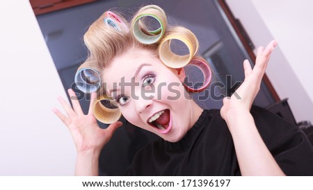 Portrait of funny happy woman in beauty salon. Cheerful blond girl with hair curlers rollers by hairdresser. Hairstyle.