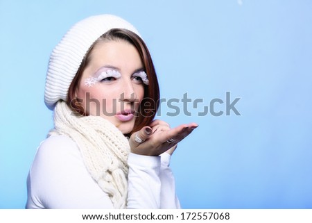 winter fashion beautiful woman in warm clothing stylish creative make up false long white eye lashes blowing a kiss blue background