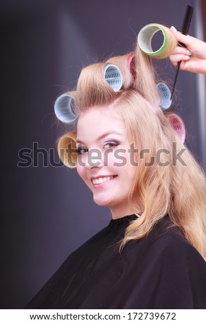 Beautiful young woman in beauty salon. Blond smiling girl with hair curlers rollers by hairdresser. Hairstyle.