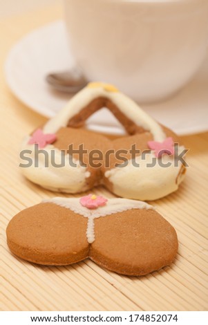 White cup and funny bikini underwear shape gingerbread cake cookie sweet dessert with yellow icing and pink decoration beige bamboo mat
