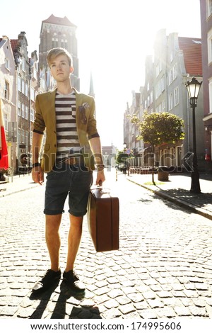 Young handsome man traveler casual style with suitcase baggage on street of old town Gdansk Poland Europe