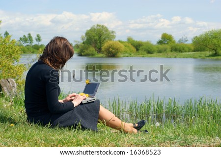 Woman typing on a laptop outside in a meadow. Blue sky with clouds. businesswoman notebook nature