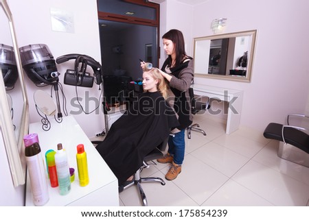 Portrait of happy woman in beauty salon. Blond girl with hair curlers rollers by hairdresser. Hairstyle.