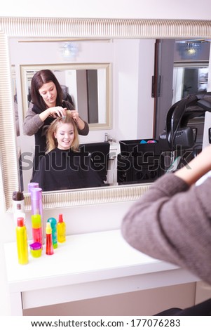 Beautiful young woman in beauty salon. Blond girl with hair curlers rollers by hairdresser. Hairstyle. Reflection in mirror.