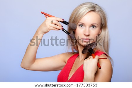 Portrait of blond girl holding professional makeup brushes on violet. Young woman as makeup artist or stylist. Studio shot.