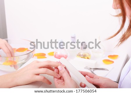 Beautician with file filing nails female client. Woman spa beauty salon