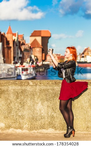 Female photographer taking pictures. Traveler woman red haired fashion girl with camera outdoors in european city, old town Gdansk river Motlawa in the background, Poland Europe