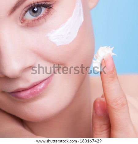 Skincare habits. Part of face of young woman as symbol of red capillary skin on blue. Girl taking care of her dry complexion applying moisturizing cream. Beauty treatment.
