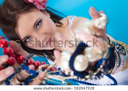 young woman fashion girl in summer style with collection of assorted jewellery, variety of beads necklaces chains in hands on blue background