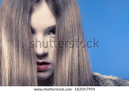 Depression. Portrait of sad emotional girl. Young woman covering her face with long hair on blue. Studio shot.