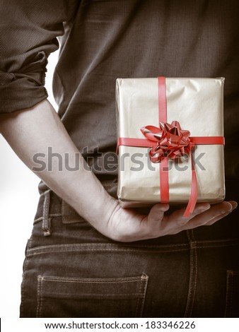 Holiday and special occasion. Closeup of male hands. Man giving golden gift box with red ribbon isolated on white. Guy hiding present behind his back. Surprise. Studio shot.
