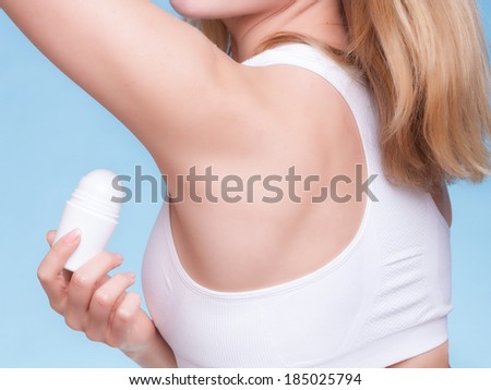 Part of female body. Girl applying stick deodorant in armpit. Young woman putting antiperspirant in underarms on blue. Daily skin care and hygiene. Studio shot.
