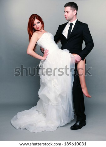 Wedding day. Portrait of happy married couple red haired sexy bride and groom in full length studio shot on gray background