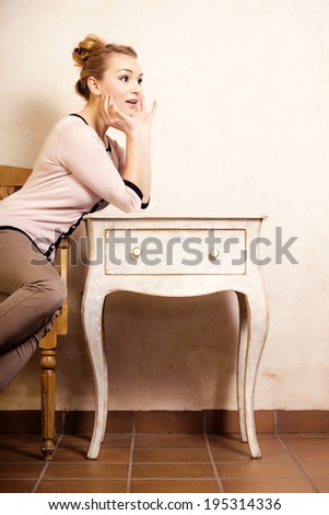 Vintage style. Full length of blond girl student or businesswoman sitting on the wooden chair at the white retro desk. Design.