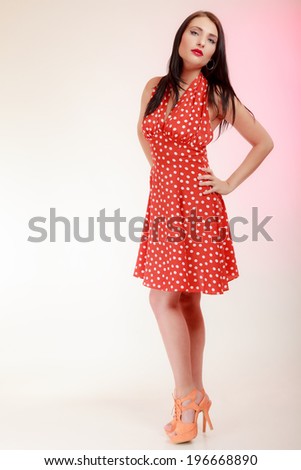 Vintage pinup style. Full length of beautiful stylized young woman. Attractive brunette girl in retro spotted red dress on pink. Disguise. Studio shot.