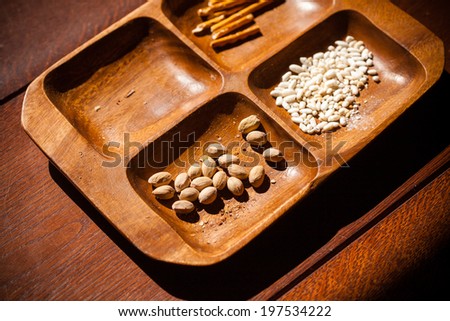 Salted mixted snacks. Closeup of pistachios nuts, roasted rice and salty sticks in brown wooden bowl. Unhealthy food.