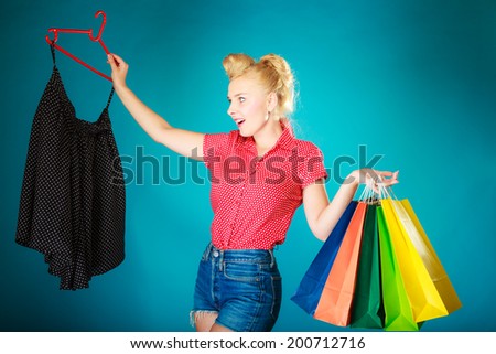 Pinup blond girl young woman in retro style buying clothes black skirt. Client customer holding colorful paper shopping bags on vibrant blue. Retail and sale. Studio shot.