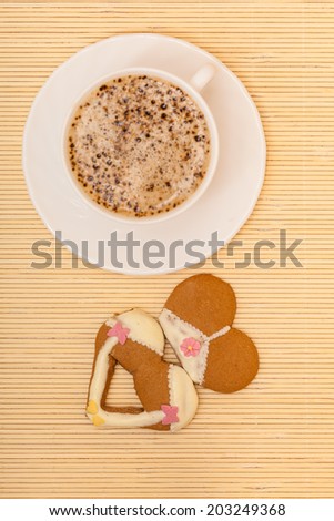 White cup of coffe with funny bikini underwear shape gingerbread cake cookie sweet dessert with yellow icing and pink decoration border or frame on beige bamboo mat