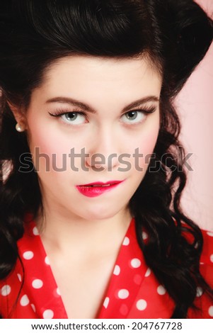 Retro style. Portrait of stylish woman biting her lips on pink. Brunette girl with pinup hairstyle and makeup.
