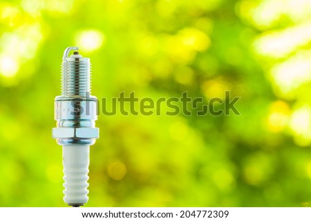 Auto service. New car spark plug as spare part of auto transportation on blurry green background.