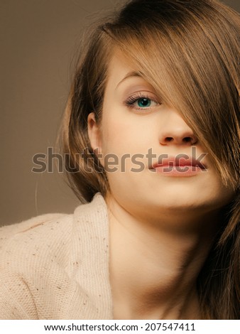 portrait of pretty sleepy girl tired young woman in beige sweater with hair fringe covered eye on brown.
