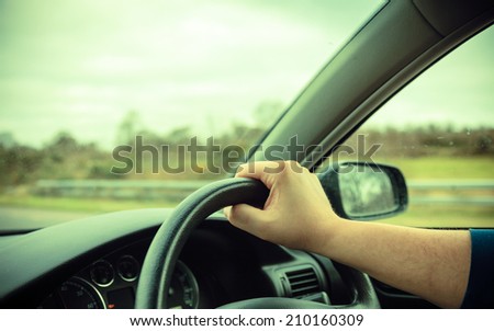 Male driver hands holding steering wheel of a car and road