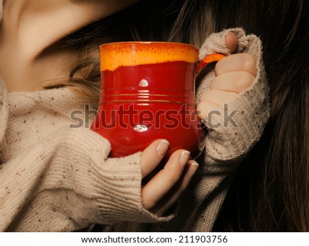 Hot beverage. Closeup of red cup mug of drink tea or coffee in female hands. Woman in warm sweater warming herself