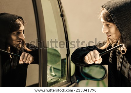 Transportation, crime and ownership concept - thief burglar breaking smashing the car window