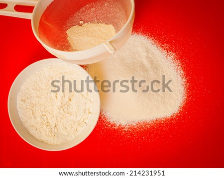 Cooking concept. Preparation for baking, bake ingredients and kitchen tools to make a cake, sifting wheat flour on red nonstick silicone mat, top view