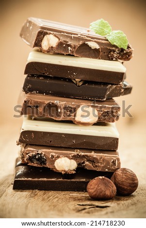 Closeup stack of different sorts chocolate pieces and hazelnuts. Variety of chocolates on wooden table.