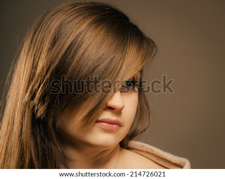 portrait of pretty sleepy girl tired young woman in beige sweater with hair fringe covered eye on brown.