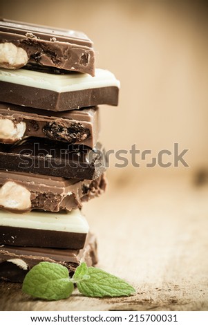 Closeup stack of different sorts chocolate pieces. Variety of chocolates on wooden table.