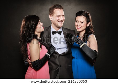 Love triangle or friendship. Portrait of two women and one man wearing elegant clothes laughing doing fun on black. Luxury party.