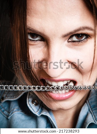 Negative emotions. Face of emotional angry woman. Portrait of mad girl biting metal chain.