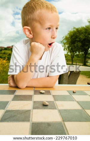 Draughts board game. Little boy clever child kid playing checkers thinking, outdoor in the park. Childhood and development