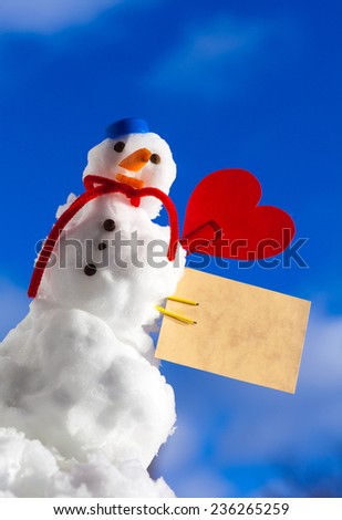 Little happy christmas snowman in blue screw top as hat red scarf and with clip red heart love symbol valentine paper card text message outdoor. Winter season seasonal specific valentine\'s day