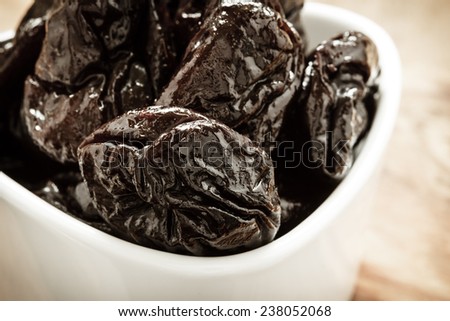 Closeup dried plums prunes fruits  in white bowl on wooden rustic table background