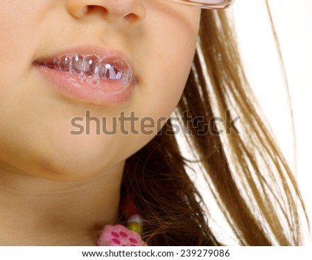 Funny little girl in glasses doing fun saliva bubbles studio shot isolated on white background