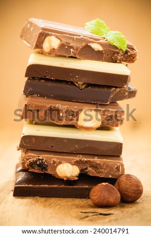 Closeup stack of different sorts chocolate pieces and hazelnuts. Variety of chocolates on wooden table.