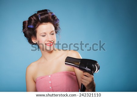Young woman preparing to party having fun, funny girl styling hair with hairdryer retro style on blue