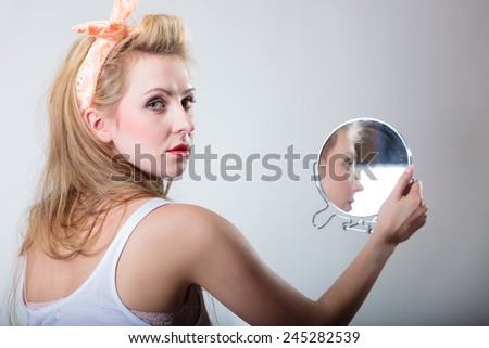 pin up beautiful blonde fashion girl in hairband looking at the mirror retro styling , studio shot gray background