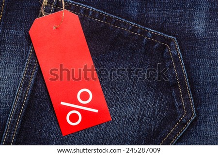 Shopping and sale concept. Closeup red label with percent sign and copy space on navy blue jeans pocket denim cotton material background